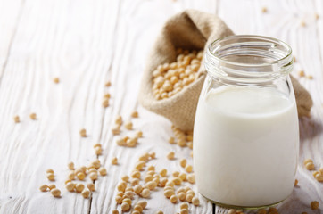 Non-dairy alternative Soy milk or yogurt in mason jar on white wooden table with soybeans in hemp...