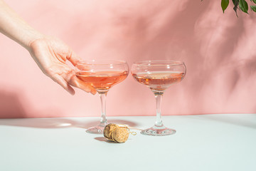 Female hand elegantly holding a glass of champagne or wine delicate pink background bright sunlight. Concept minimalism.