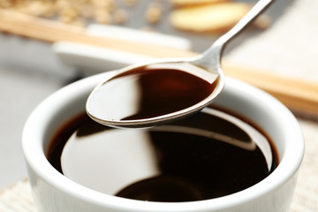 Spoon with soy sauce over bowl, closeup