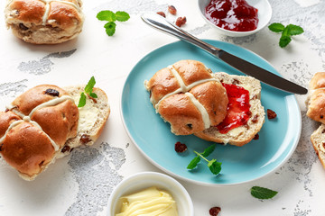 Hot cross buns in blue plate served with butter, strawberry jam and cup of tea