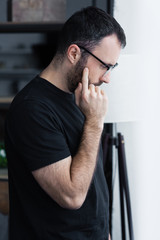 side view of upset man in black t-shirt and glasses holding hand near face