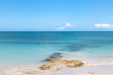 Rocks on an Antiguan beach, with a turquoise sea behind and blue sky overhead