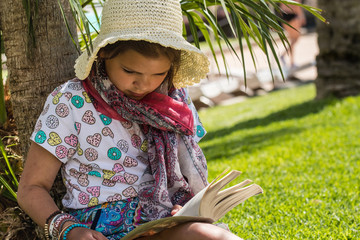 Podczas wakacji dziewczynka czyta ciekawą książkę w cieniu drzew - obrazy, fototapety, plakaty