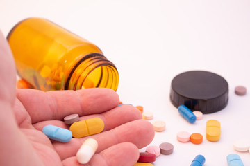 Medications in the form of pills and capsules on a white background. Hand of a man holding colored pills.