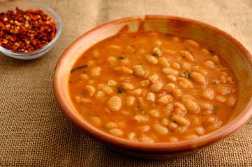 Plate of traditional greek bean soup on sackcloth, served with crushed red pepper