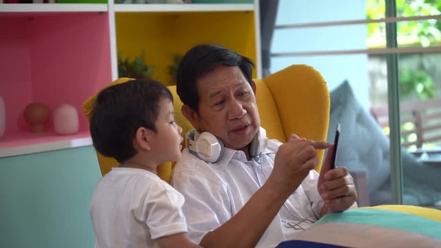 happy Grandfather and grandson Sharing smartphone together listening to music with headphone enjoying on sofa or couch in living room at home family.grandpa,grandchildren,relationship.technology