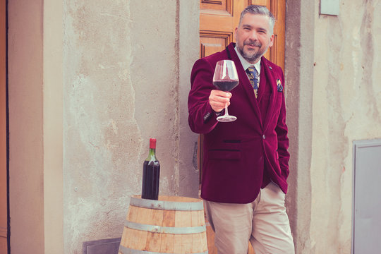 Confident elegant dressed man with glass of red wine standing outdoors