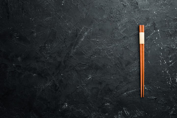 Wooden chopsticks on a black stone background. Top view. Free space for your text.