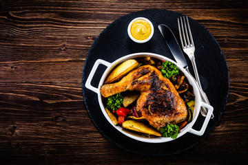 Grilled chicken legs with baked potatoes and vegetable salad on black stone plate