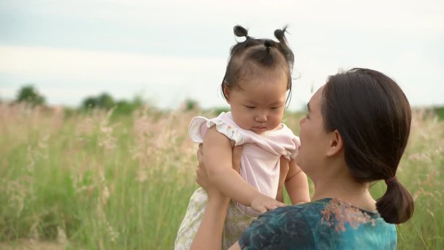 Asian young mother and daughter in the grass field at sunset, Handheld shot 4K.