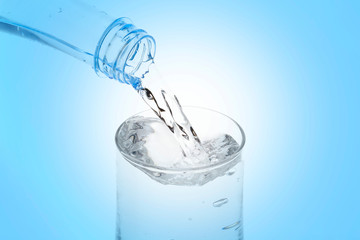Pouring water from bottle into glass on blue background