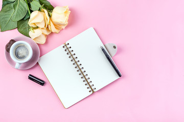 Morning coffee mug for breakfast, empty notebook, pencil and rose on pink table top view . Woman working desk.