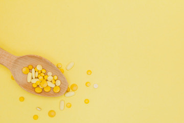 Yellow round vitamin pills in spoon on a yellow background, copy space