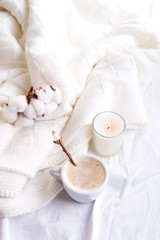 Obraz na płótnie Canvas Bedding with a fluffy knitted plaid and cup of coffee, cotton flowers and candle. Cozy day. Flat lay, top view