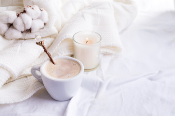 Obraz na płótnie Canvas Bedding with a fluffy knitted plaid and cup of coffee, cotton flowers and candle. Cozy day. Flat lay, top view