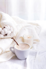 Fototapeta na wymiar Bedding with a fluffy knitted plaid and cup of coffee, cotton flowers and candle. Cozy day. Flat lay, top view