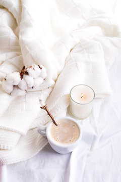 Bedding with a fluffy knitted plaid and cup of coffee, cotton flowers and candle. Cozy day. Flat lay, top view
