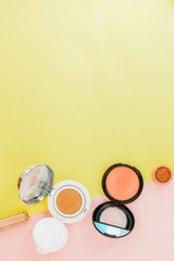 Make up products spilling on to a bright yellow and pink background with copy space
