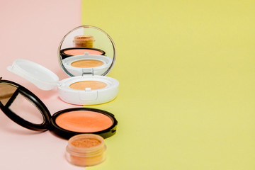 Make up products spilling on to a bright yellow and pink background with copy space