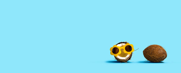 Coconut wearing sunglasses and coconut shell on a solid background
