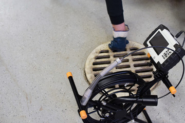 Sewer inspection camera. Man removing drainage grill on background.