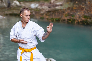 Strong athletic young male master of martial arts in white karate suit with a yellow belt engaged...