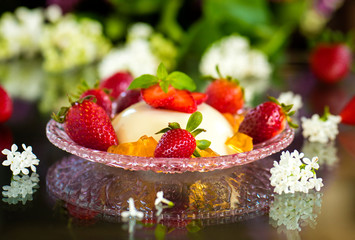 Panna Cotta with strawberries on a dark background with flowers