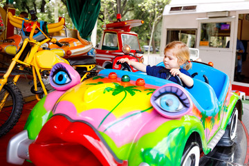 Adorable little toddler girl riding on funny car on roundabout carousel in amusement park. Happy healthy baby child having fun outdoors on sunny day. Family weekend or vacations © Irina Schmidt