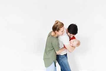 Concert of successful young family - father holding on the hands of small laughing child next to positive young mother on a white background. Space for text