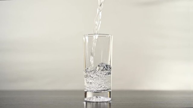 Pouring water into a glassPouring glass of water in slow motion. A tall transparent glass receptacle filling with the lifeblood of the earth.