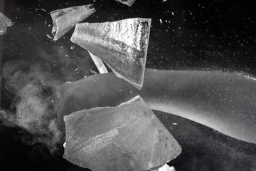 Moody, Shadowy High-Speed Photo of a Caucasian Man's Bare Fist Smashing through a Sheet of Ice - Exploding in a Cloud of Dust and Shards with a Black Background