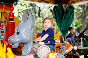 Adorable little toddler girl riding on animal on roundabout carousel in amusement park. Happy healthy baby child having fun outdoors on sunny day. Family weekend or vacations © Irina Schmidt