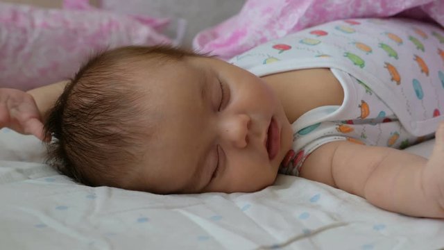 Newborn baby sleeping on a bed and flinching. Reflex moro newborns.