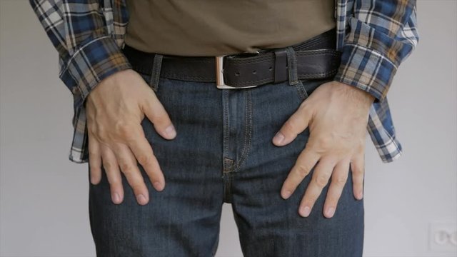 The man standing in front of a white wall examines the contents of their pockets of trousers, flapping her hands in the pockets and tucking in their hands