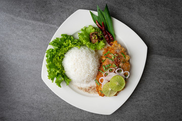Spicy salad with fried chicken and rice in white dish on table.