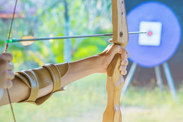 Tourists try to use a bow and arrow and shoot at a target in the amusement park.
