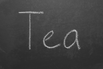 Hand-written lettering with chalk "tea" on a gray board
