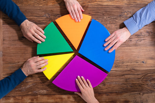 Businesspeople Holding Multicolored Pie Chart Over Desk