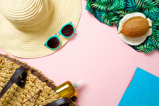 Women's beach accessories: straw hat, sunglasses, coconut, paper notebook, beach bag with essential oil on pink background. Traveler stuff concept, summer background. Flat lay composition, top view.