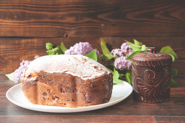 A baked homemade cake dusted with powder stands on a board near a small clay pot. Nearby is a knife. On wooden background