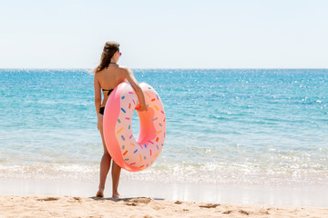 Naklejka na ściany i meble A woman walks into the sea water. Girl relaxing on inflatable ring on the beach. Summer holidays and vacation concept