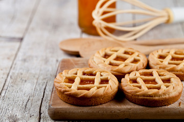 Fresh baked tarts with marmalade or apricot jam filling and on ceramic plate and kitchen bakery utensil.