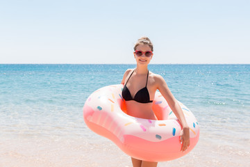 Beautiful young woman in swimming pool swims on inflatable ring donut and has fun with glass of cocktail on vacation