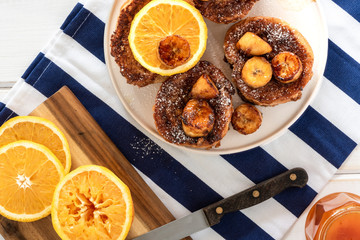 French toast with fried bananas and orange sauce. Top view, light background.