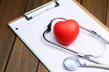 Red heart with stethoscope and electrocardiogram on wooden background