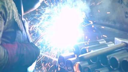 Industrial worker in protective mask using modern welding machine for welding metal construction on production manufacture at metalworking factory