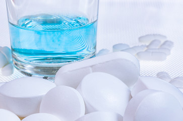 Nahaufnahme von weißen Tabletten mit einem Wasserglas im Hintergrund