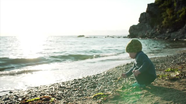 Cute 1,5 years old boy is playing with rocks and shells at Ritz bay seaside beach, Nakhodka, Russia. Evening