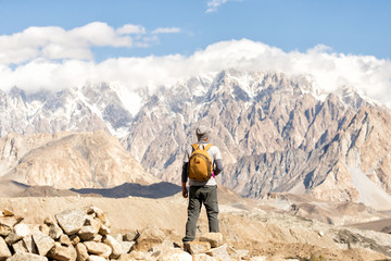 Asian men are tourists carrying backpacks, standing back, looking at the peak of passu on a clear day. During the autumn in hunza village in Pakistan