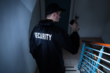 Male Security Guard Standing On Staircase Holding Flashlight